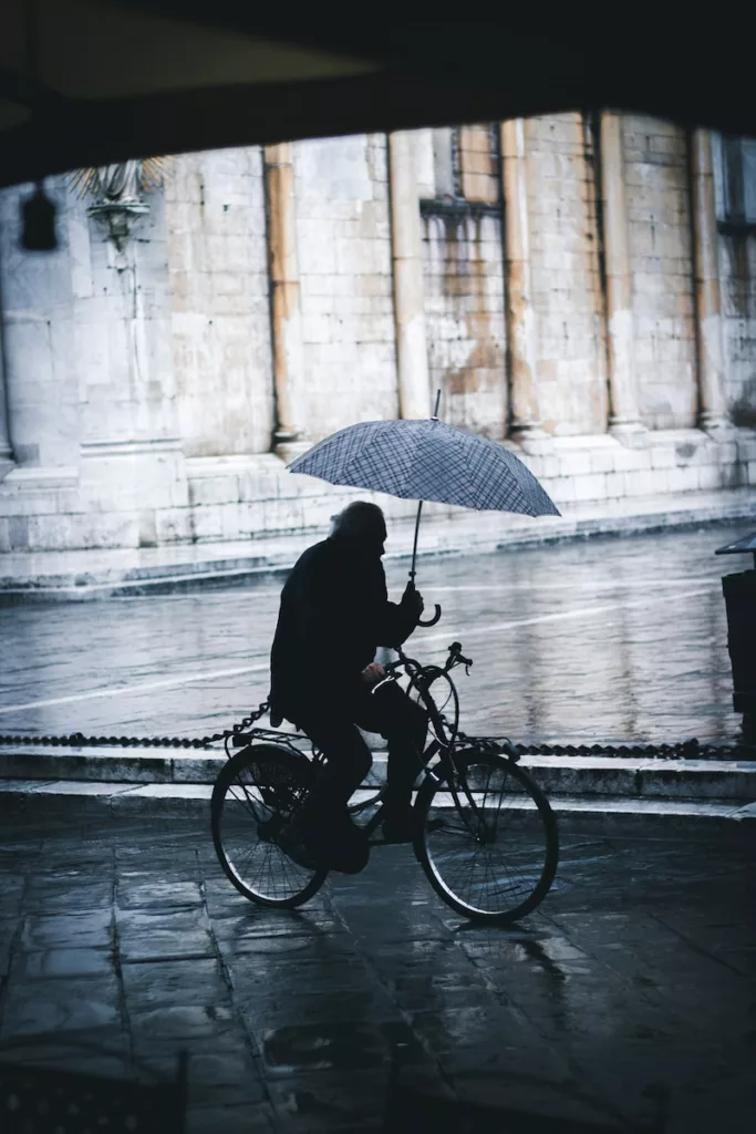 man riding bicycle while holding umbrella near street