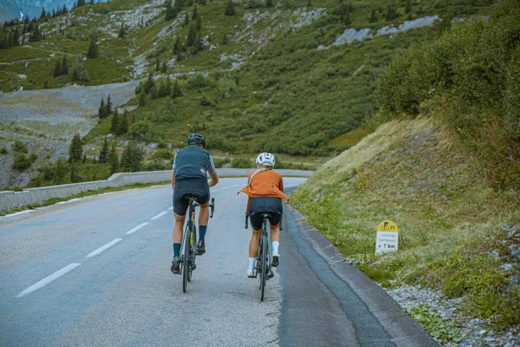 a couple of people riding bikes down a road in the alps