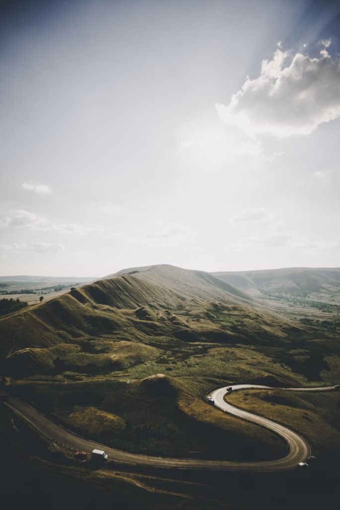 peak district aerial photography of vehicle arriving on concrete road near mountains under white clouds at daytime