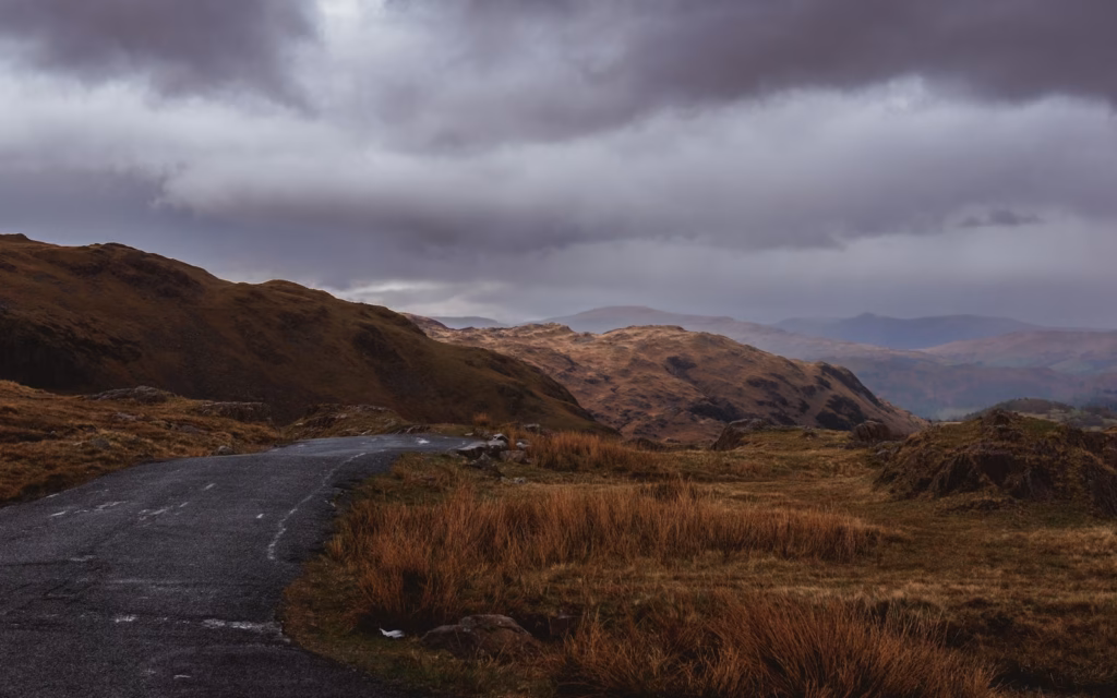 wrynose passa road in the middle of a field with mountains in the background