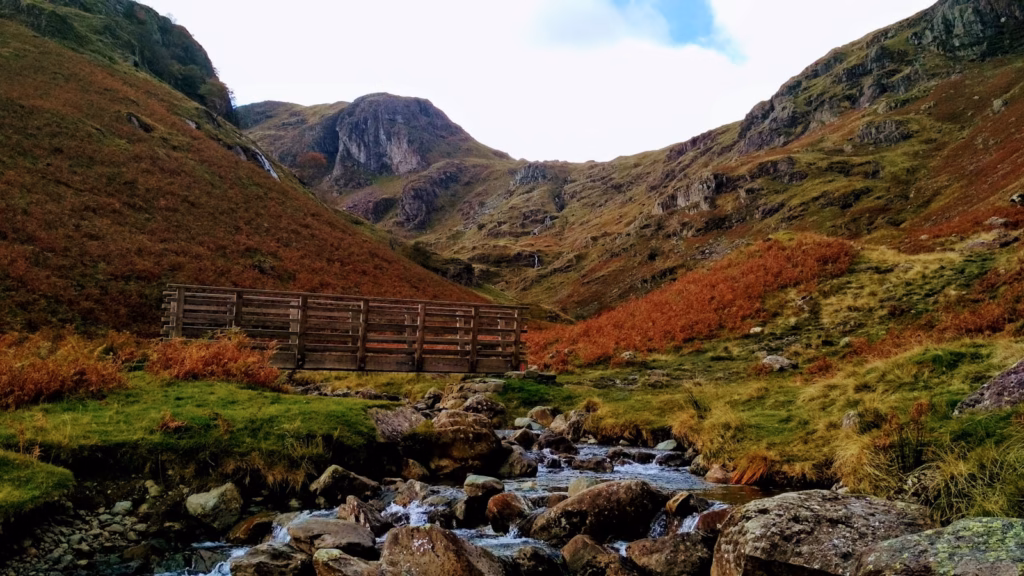 Lake District brown wooden bridge over river near brown mountains during daytime