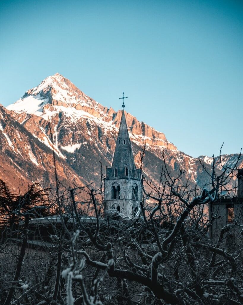 Martigny A church with a steeple in front of a mountain