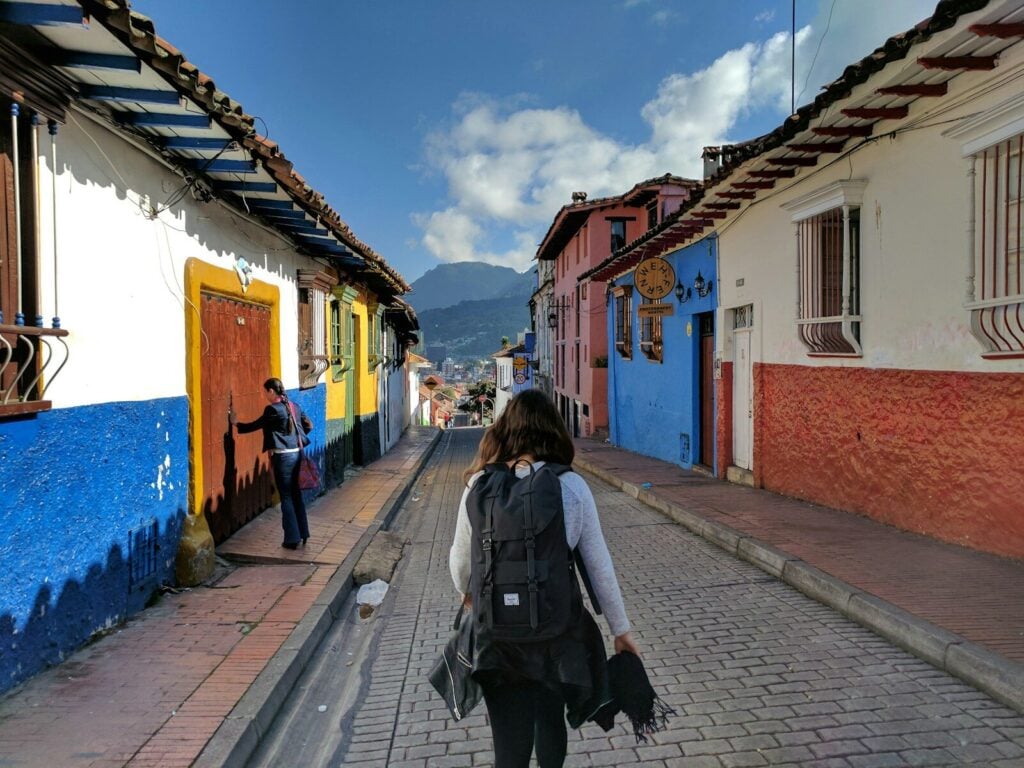 Bogota person in gray shirt with backpack walking on street between houses
